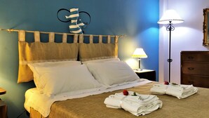 A neatly made bed with white linens, a striped pillow, and a rose on the bed. There is a lamp on a bedside table and a wooden dresser in the room. - Stella del Mare (Monopoli)