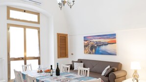 A dining area with a table set for two, a sofa, and a painting of a cityscape. - Donna Lisa (Polignano a Mare)