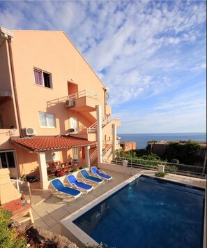 A two-story building with a swimming pool, outdoor seating, and a view of the sea. - Apartman Ana Cavtat (Konavle)