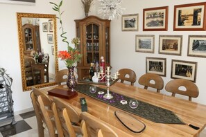 A dining area with a wooden table, chairs, a vase with flowers, a candelabra, and framed pictures on the wall.