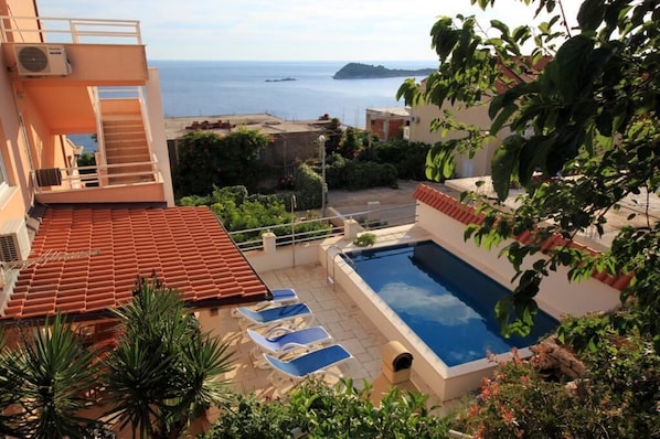 Enjoy a refreshing swim with a view of the sea and a distant island from our rooftop pool, surrounded by lounge chairs on a spacious deck.