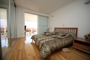 A bedroom with a large bed, wooden flooring, a nightstand, and a sliding glass door leading to a balcony. - Apartman Ana Cavtat (Konavle)