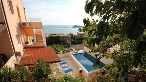 Un espace piscine avec vue sur la mer, un toit recouvert de tuiles rouges et un escalier menant à un balcon.