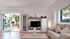 A modern living room with a flat-screen TV, a sofa, a coffee table, and a sliding glass door leading to an outdoor area. - Villa with pool and sea view - Villa Rica (MENORCA)