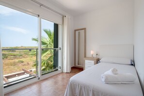 A bedroom with a large sliding glass door, a bed with a white bedspread, a nightstand with a lamp, and a view of the landscape. - Villa with pool and sea view - Villa Rica (MENORCA)