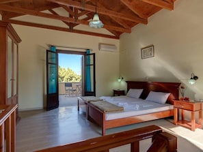 A bedroom with a wooden bed, a nightstand, a desk, and a chair. There is a balcony with a view of trees. - Group Accomodation, Heliopetra Studios And Houses (Apokoronas)