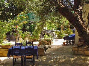 An outdoor patio with tables and chairs, surrounded by greenery and stone walls. - Group Accomodation, Heliopetra Studios And Houses (Apokoronas)
