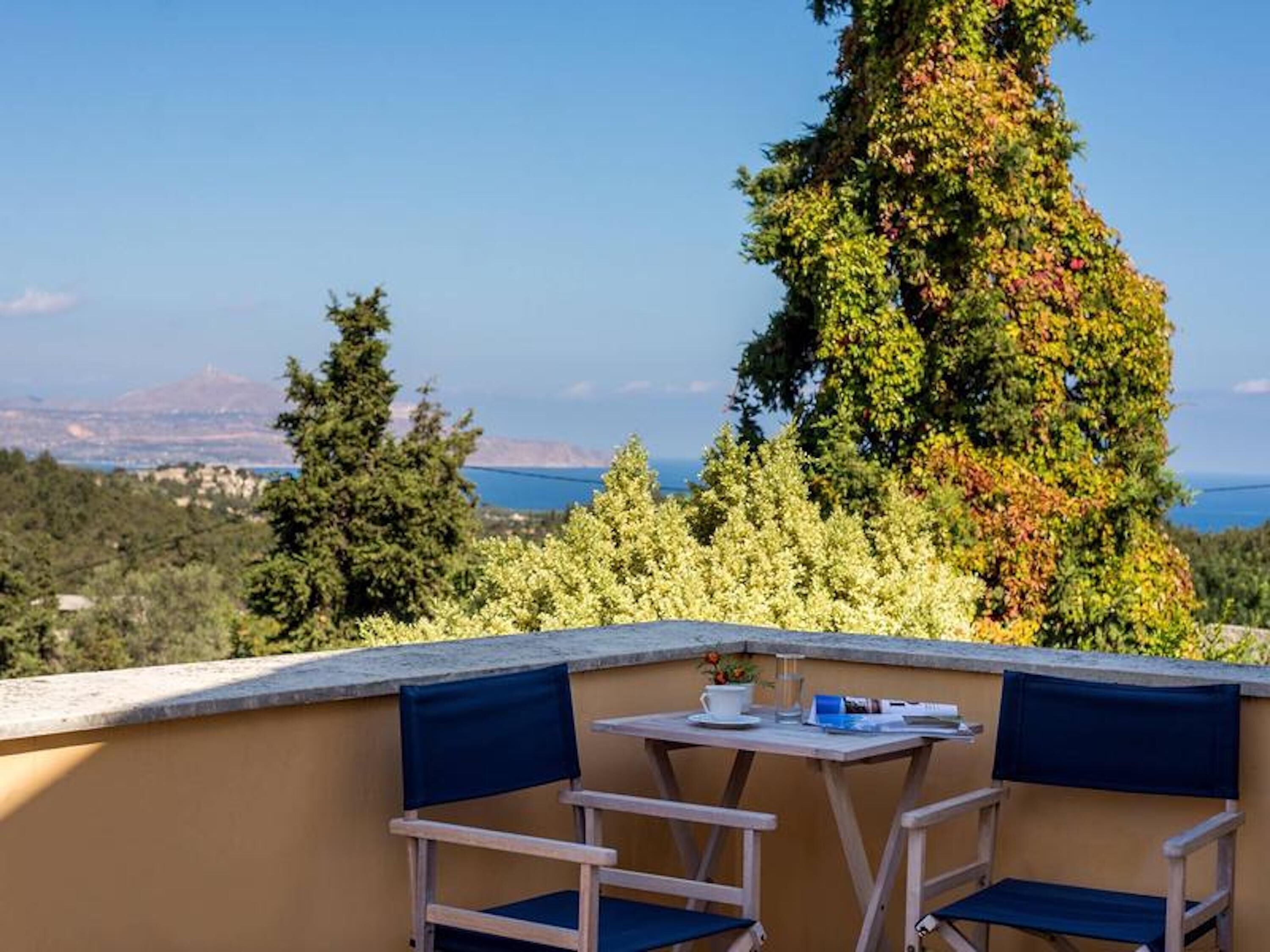 A terrace with two chairs and a table, overlooking a scenic landscape with trees and a view of the sea.