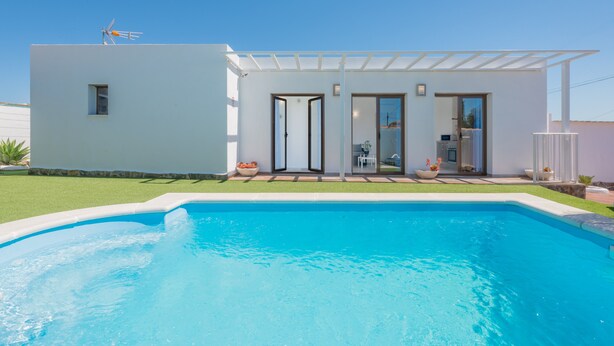 Una casa moderna con piscina, patio y cielo despejado.