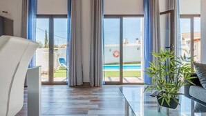 Una sala de estar moderna con una mesa de centro de vidrio, un sofá y vistas a una piscina.
