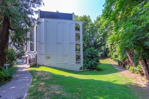 A modern building with a curved facade, a paved pathway, and lush greenery surrounding it. - Maraini Elegante (Lugano)