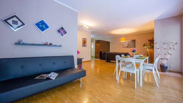 Una sala de estar moderna con un sofá oscuro, una mesa de comedor con sillas y una cocina al fondo.