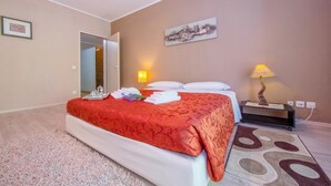 Habitación de hotel con cama, mesita de noche, lámpara, un cuadro en la pared y una puerta que da a otra habitación.
