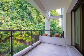 Un balcón con vistas a abundante vegetación y una ventana con cortina.
