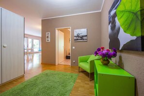 A modern living room with a green sofa, a green side table with a vase of flowers, a green rug, and a large wall mural. - Maraini Elegante (Lugano)
