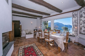 Zona pranzo con tavolo apparecchiato per quattro, sedie di legno, tappeto rosso a motivi e vista sulle montagne attraverso una finestra.