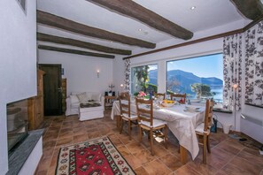 A dining area with a table set for four, wooden chairs, a red patterned rug, and a view of mountains through a large window. - Morcote Magic View (Morcote)
