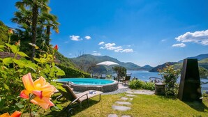 A pool area with lounge chairs, a stone pathway, and a view of mountains and water. - Morcote Magic View (Morcote)