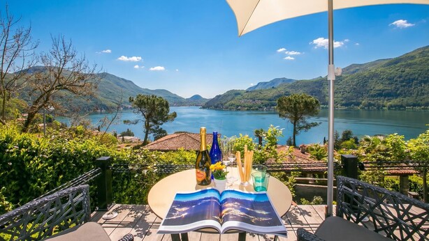 A table with a book, a bottle, and glasses, overlooking a lake and mountains. - Morcote Magic View (Morcote)