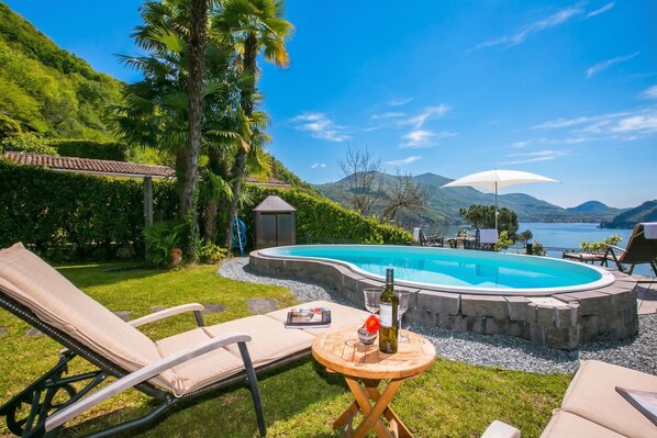 A poolside area with lounge chairs, a table with a bottle and glasses, and a view of mountains and water. - Morcote Magic View (Morcote)
