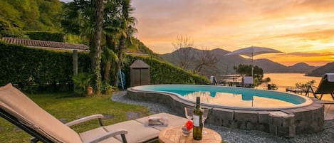Una piscina con sillones reclinables y una mesa, rodeada de vegetación y colinas.