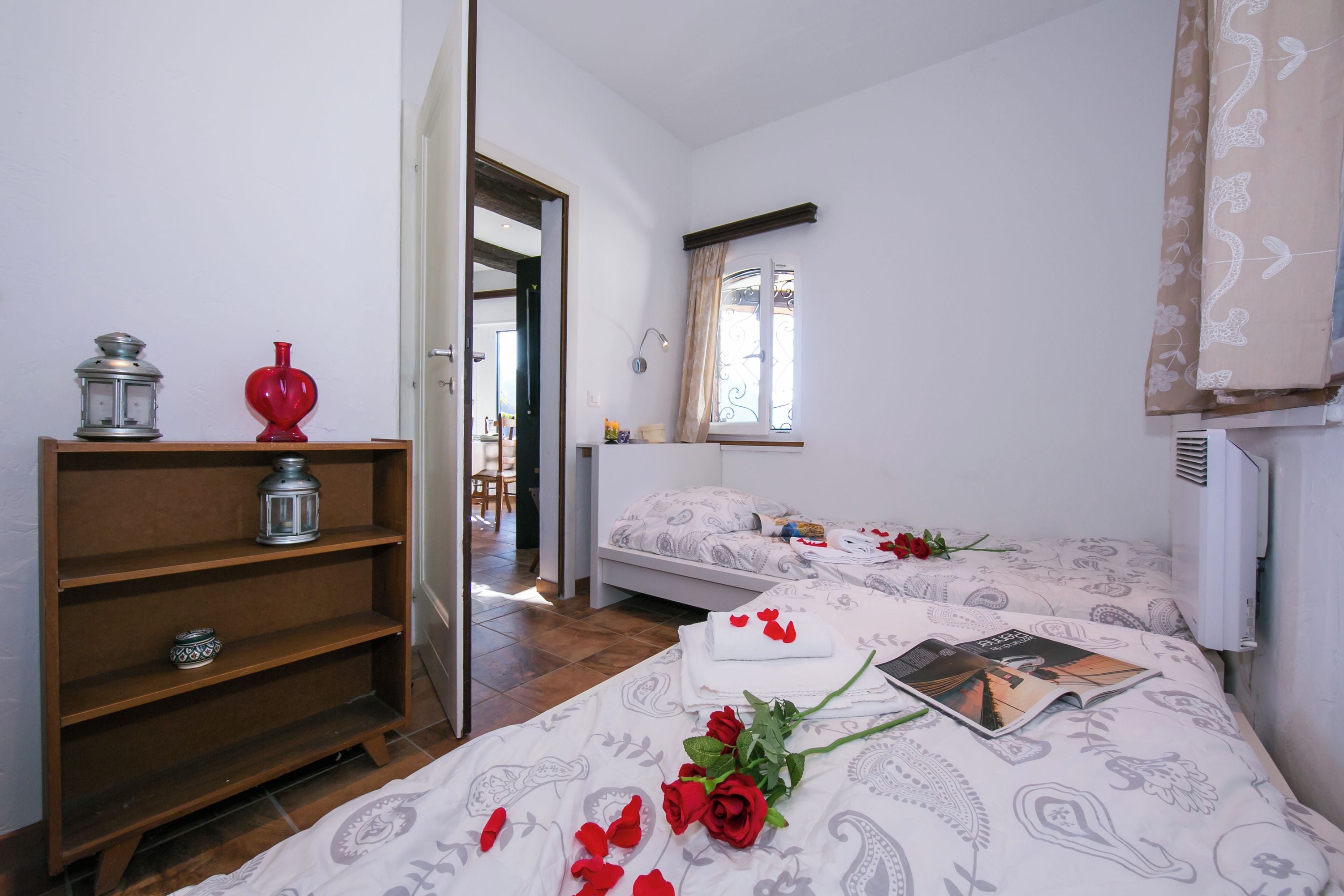A bedroom with two beds, a wooden shelf, and a window with curtains.