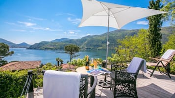 A deck with outdoor furniture, a table with a bottle and glasses, and a view of a lake and mountains.