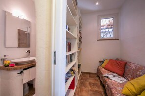 A bathroom with a sink, mirror, and shelves, a window with a view, and a sofa with cushions. - Morcote Magic View (Morcote)