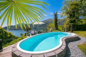 A swimming pool with a curved edge, surrounded by a stone deck, with a view of a lake and mountains in the background. - Morcote Magic View (Morcote)