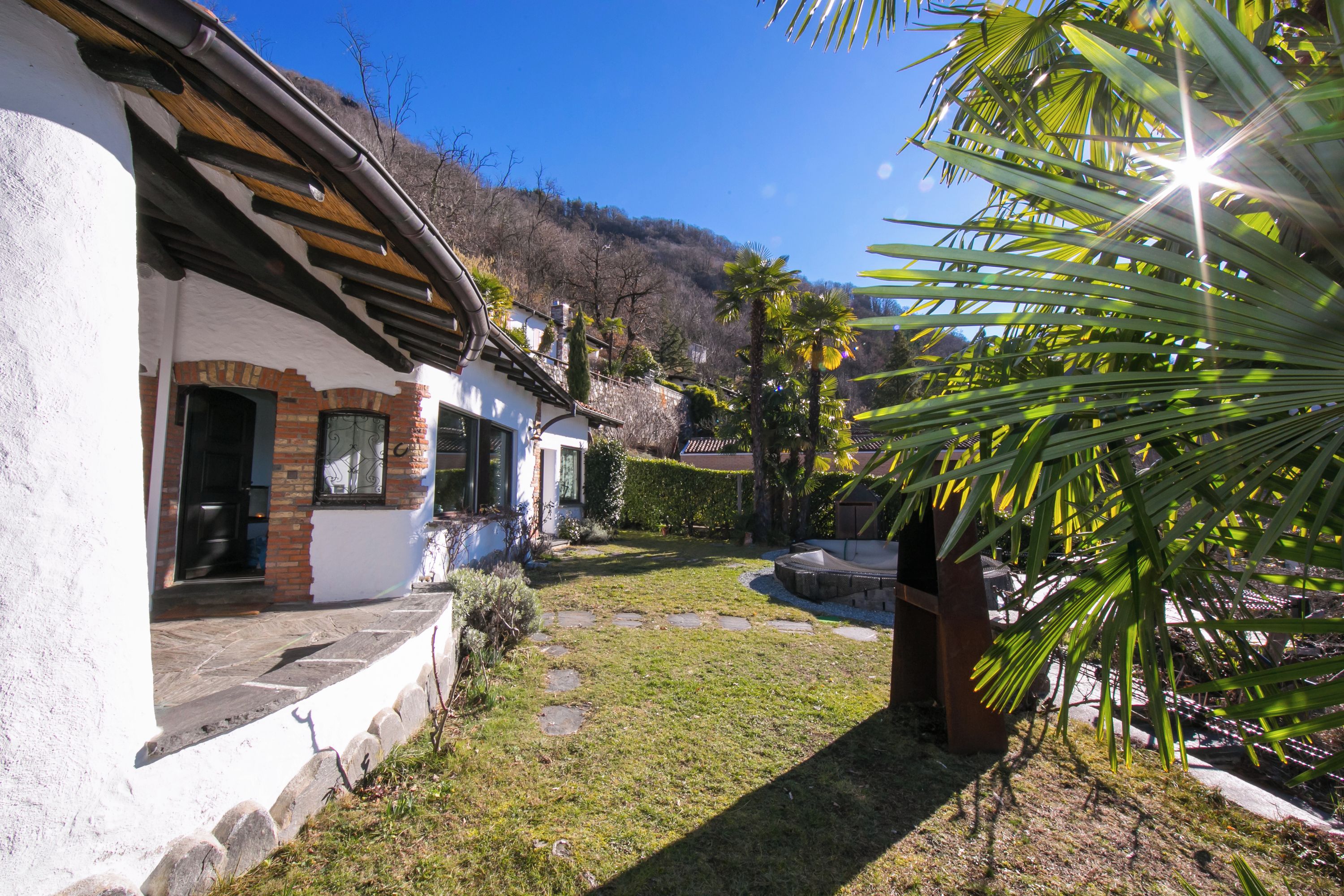 A traditional building with a stone facade, a wooden roof, and a small garden with palm trees.