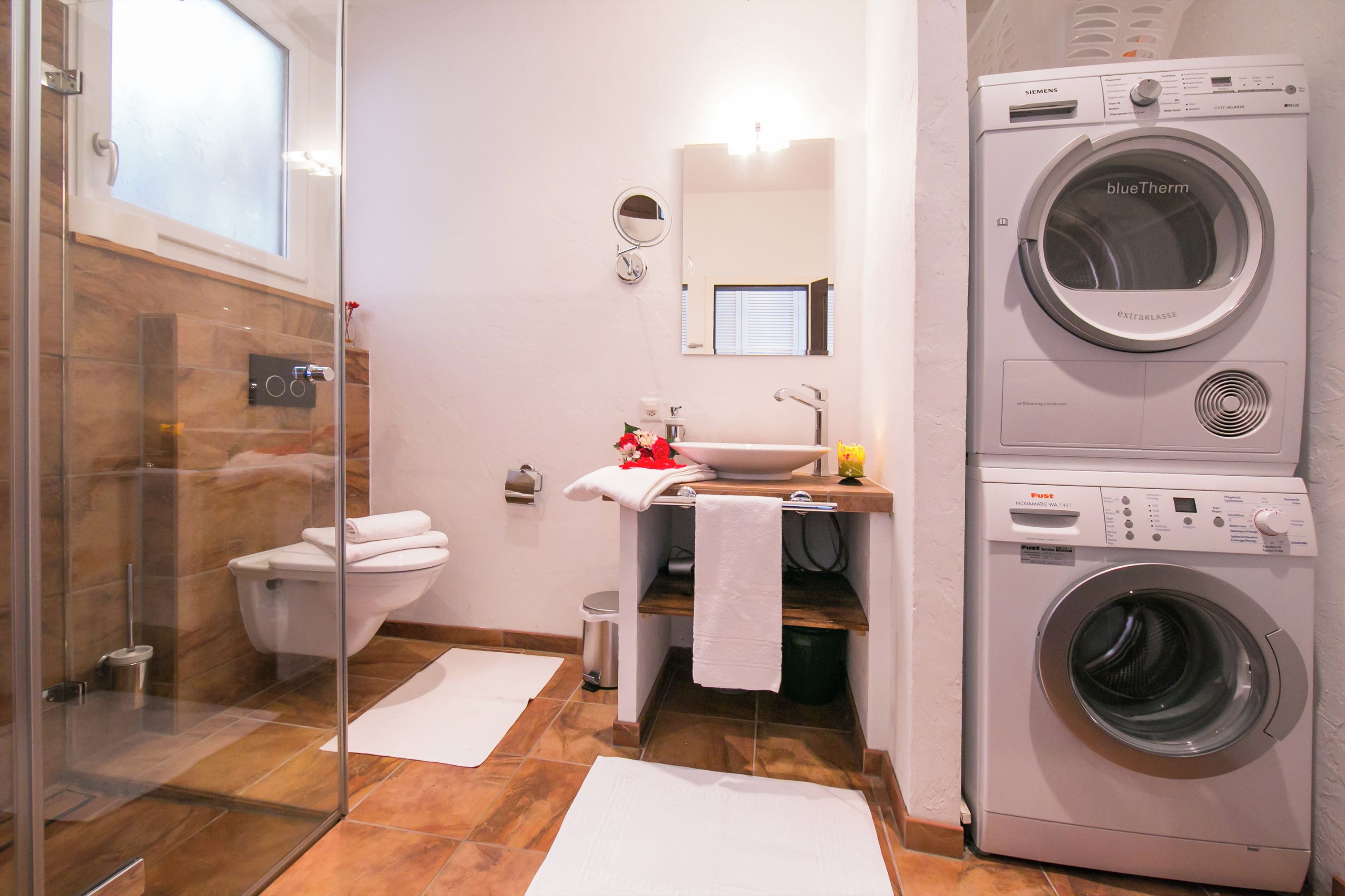 A bathroom with a glass shower enclosure, a toilet, a sink with a mirror, and a stacked washer and dryer.