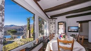 A dining area with a view of a lake and mountains, wooden furniture, and a table set for two. - Morcote Magic View (Morcote)