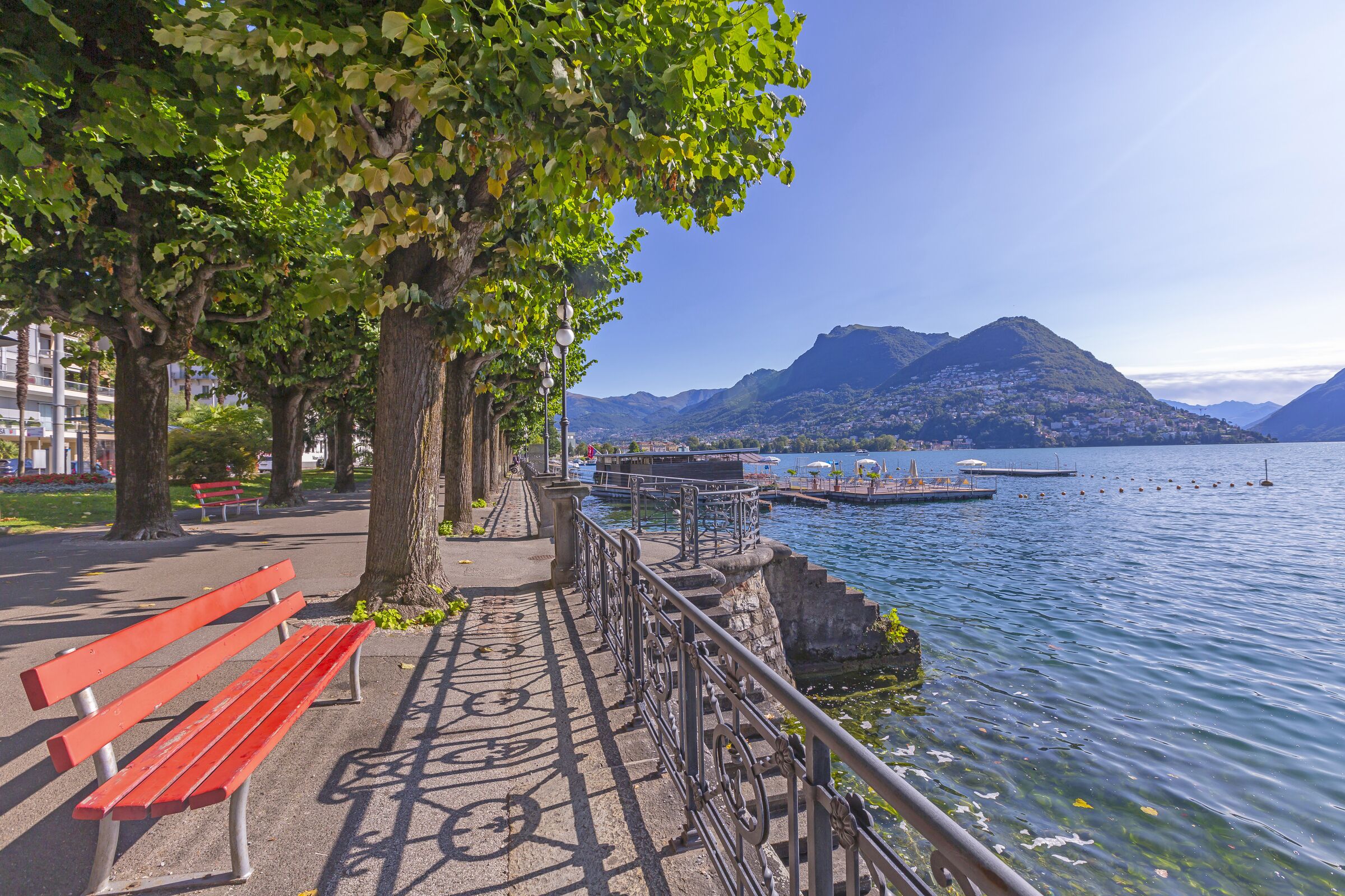 Une promenade au bord du lac, agrémentée de bancs, d’une rambarde et offrant une vue sur une montagne et un lac.