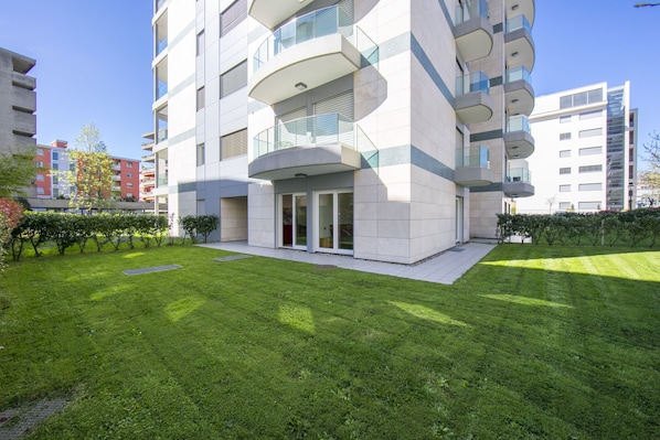 A modern apartment building with balconies, a well-maintained lawn, and a clear sky.