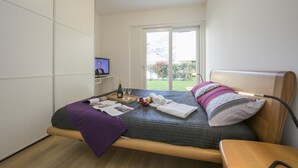 A modern bedroom with a large bed, a television, and a sliding glass door to a balcony. - Prestige du Lac 4 (Lugano)