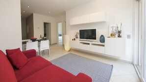 A modern living room with a red sofa, a flat-screen TV, and a dining area with white chairs and a table. - Prestige du Lac 4 (Lugano)