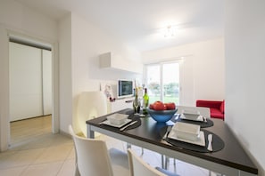 A modern dining area with a dark table, white chairs, and a bowl of fruit.