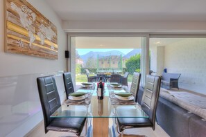 A dining area with a glass table, leather chairs, and a view of mountains through a sliding glass door.