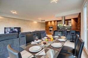 Un comedor moderno con una mesa de vidrio dispuesta para cuatro personas, un sofá y una cocina al fondo.
