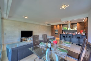 A modern living room with a glass dining table, sofas, and a TV. - Rebecca Garden (Lugano)