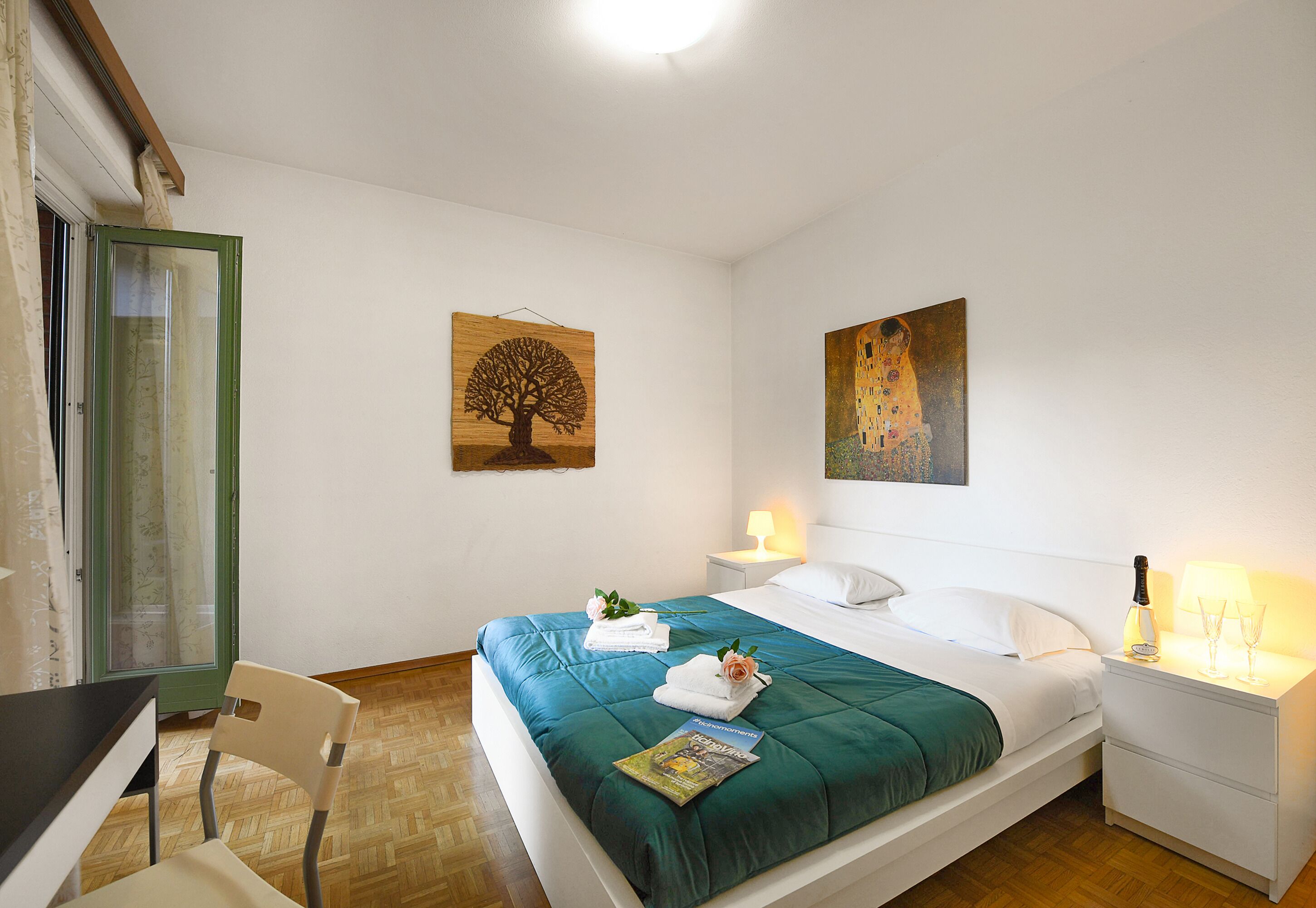 Une chambre d’hôtel bien rangée, avec un lit, une chaise, une table de chevet et deux tableaux accrochés au mur.