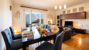 A modern living room with a dining area, a fireplace, and a view of mountains. - Santiago Home (Lugano)