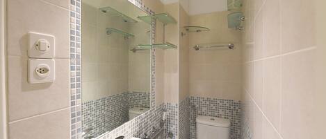 A bathroom with a white sink, mirror, and toilet. There are glass shelves above the sink and a shower area with a glass door.