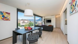 A modern living room with a dining area, large windows, and a view of buildings and mountains. - Urban Flat Paradiso (Paradiso)