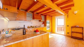 A kitchen with wooden beams, a marble countertop, and a view to the outside.