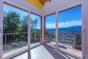 A balcony with glass doors, a tiled floor, and a view of a city and mountains. - Lugano Panoramica (Lugano)