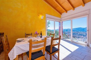 Un coin repas avec une table dressée pour quatre personnes, des chaises en bois, une nappe blanche et une vue sur le paysage urbain à travers de grandes fenêtres.