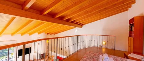 A spacious room with a wooden ceiling, a balcony, a fireplace, and a bed with towels.