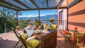 A terrace with a table set for dining, potted plants, and a view of mountains. - Lugano Panoramica (Lugano)