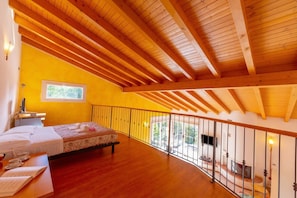 Un dormitorio con techo de madera, una cama, un escritorio con silla, una ventana y un balcón con barandilla.